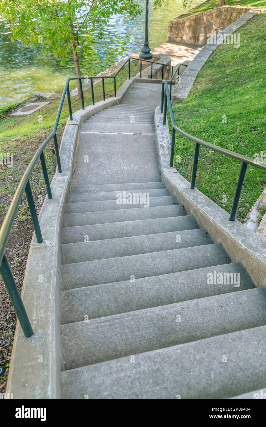 Escalier extérieur dans un parc descendant un parc pittoresque avec de l'eau ondulant. Vue depuis le sommet d'un escalier extérieur en béton avec rambardes métalliques au milieu de sc Banque D'Images