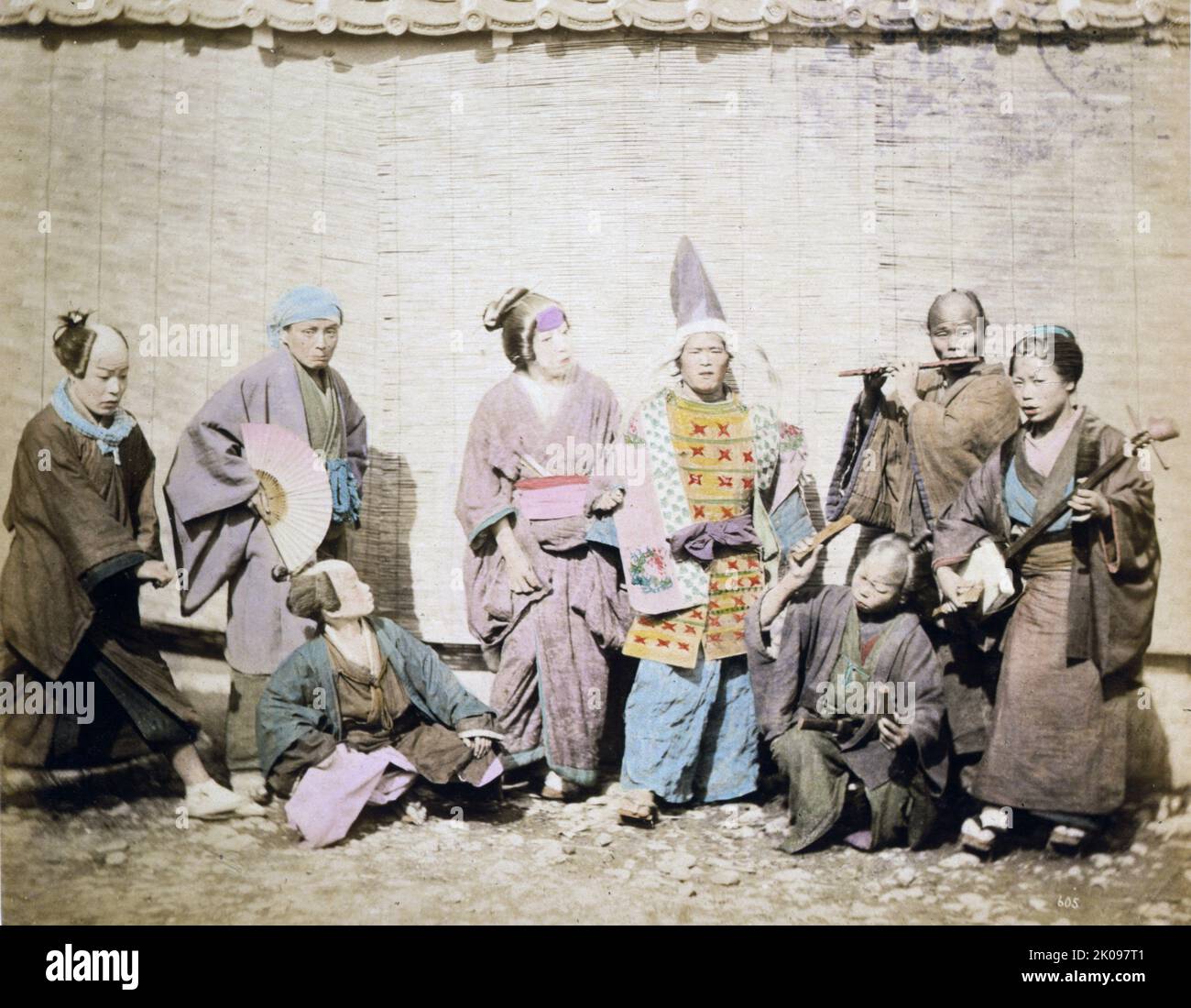 Groupe de musiciens et d'acteurs de rue devant un bâtiment avec des stores en roseau ou en bambou. Par Stillfried & Andersen, c1877. Impression photographique. Banque D'Images