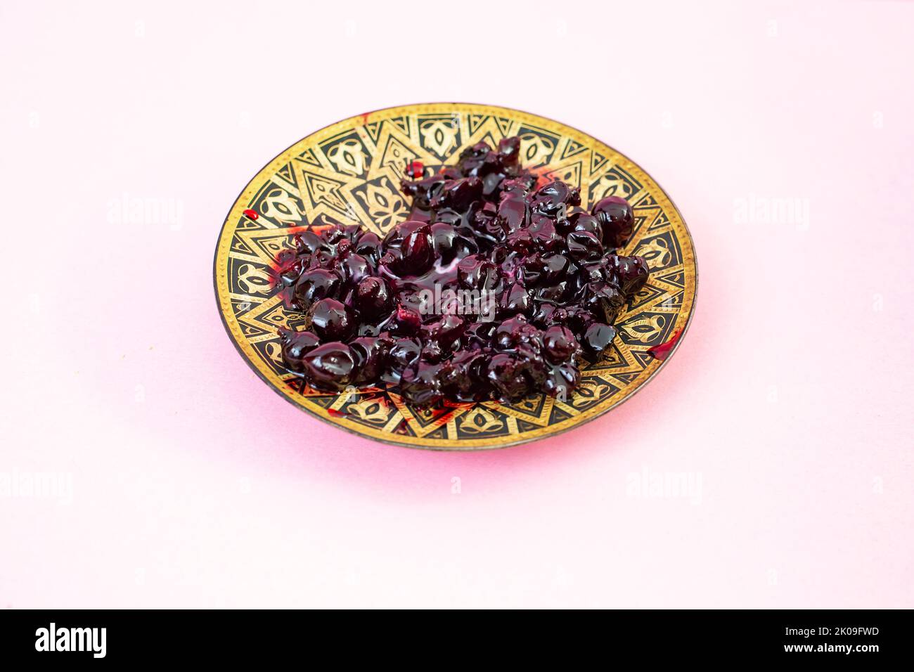 Confiture de cassis sauvage sur une plaque de métal oriental, isolée sur fond rose Banque D'Images