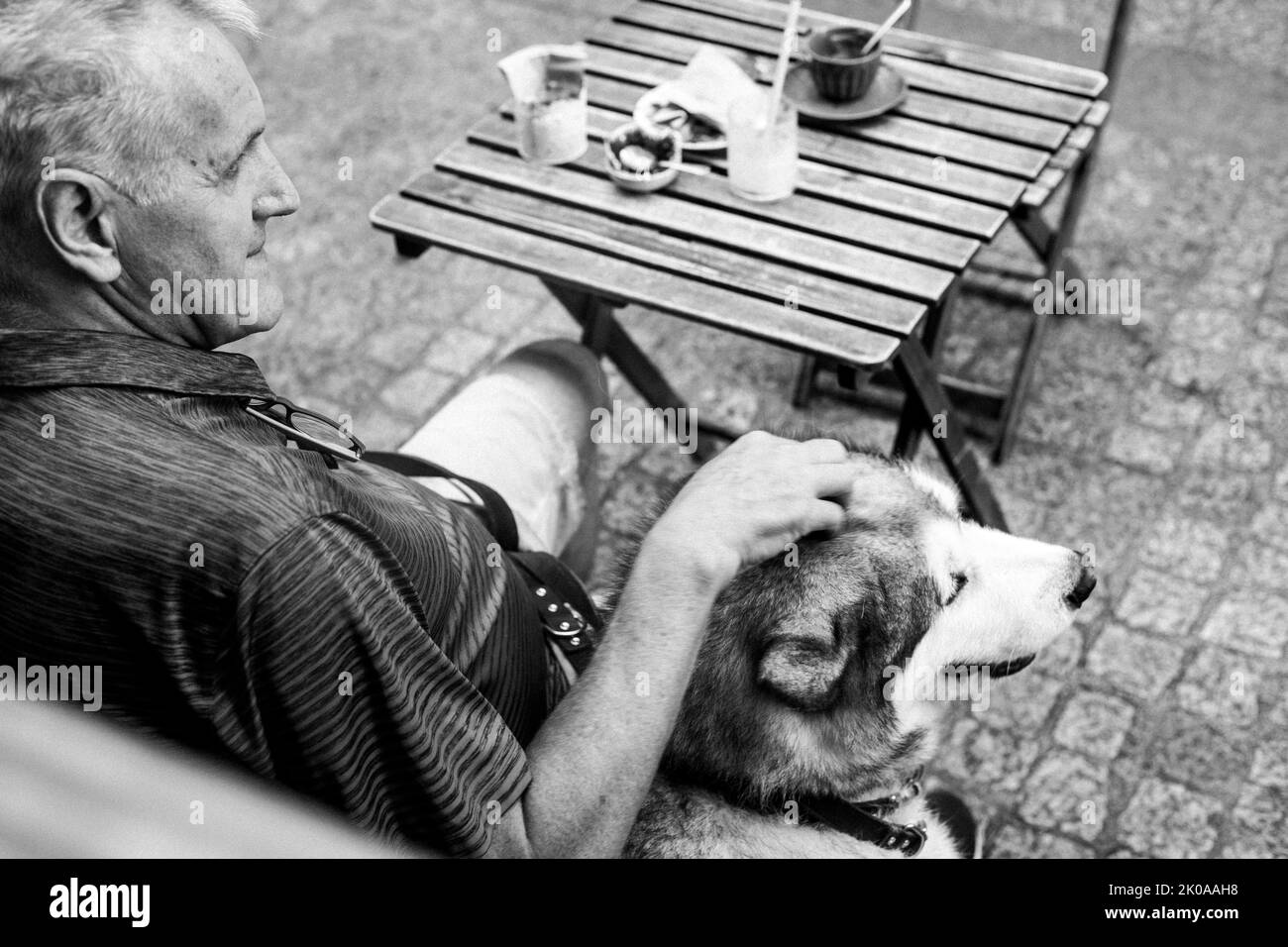 Un homme qui a caressé la tête de son chien pendant qu'il s'assoit à une table de café à l'extérieur. Banque D'Images