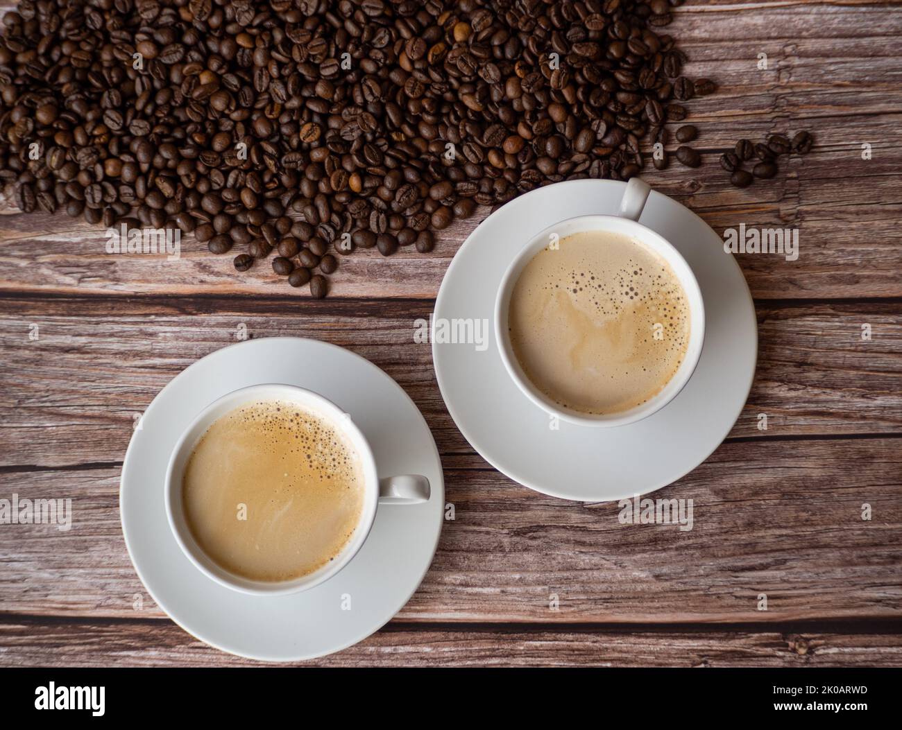 vue de dessus de deux tasses blanches avec du lait de café sur une table en bois. grains de café en arrière-plan Banque D'Images
