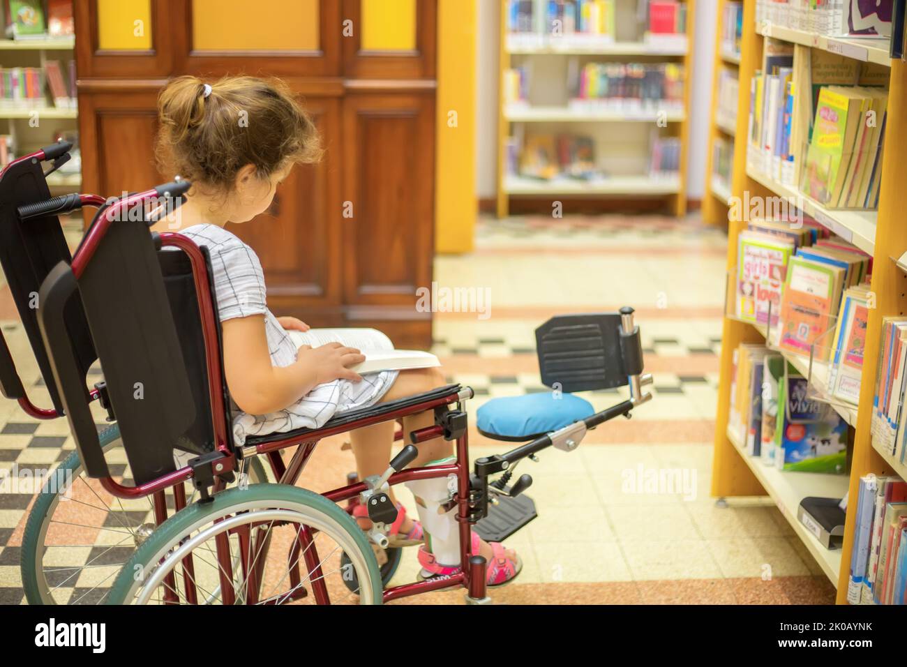 Une écolière en fauteuil roulant choisit des livres dans la bibliothèque.vie à l'âge de l'éducation des enfants ayant des besoins spéciaux.concept d'éducation d'un dis heureux Banque D'Images