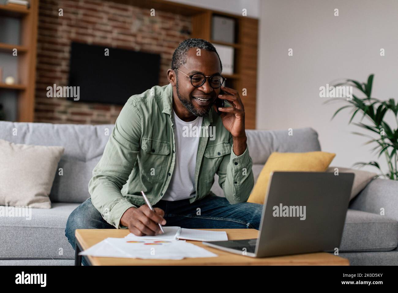 Souriant occupé mature afro-américain gars Manager dans des lunettes et décontracté, ont l'appel par téléphone, travaille sur ordinateur portable Banque D'Images