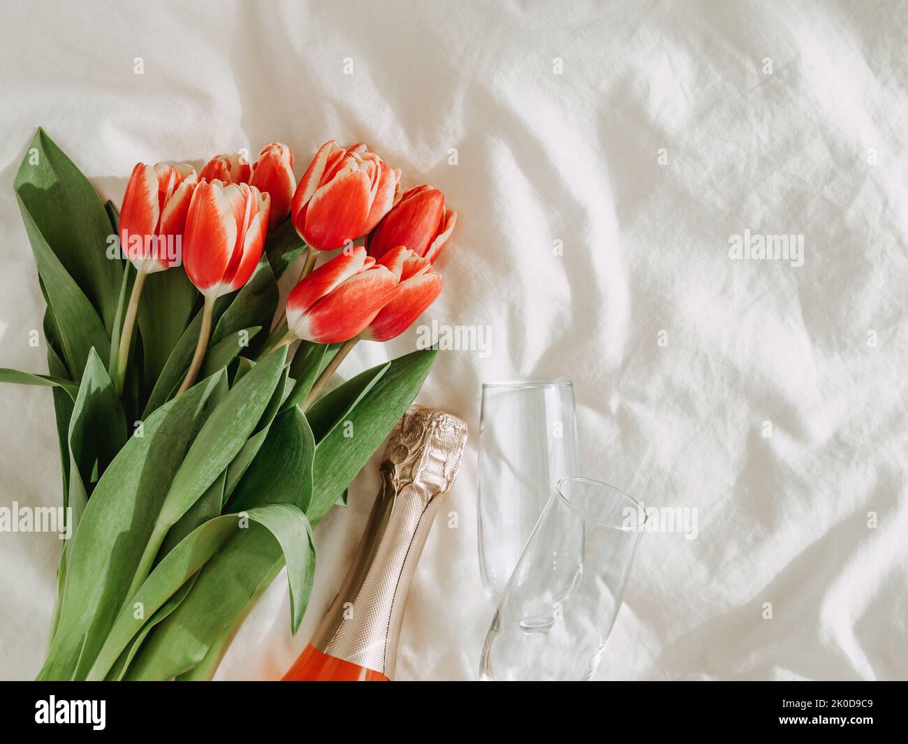Bouquet de tulipes rouges, vin de rose et verres à champagne sur draps blancs. Concept de la Saint-Valentin, date, mars 8. Fleurs de printemps et esthétique des bouteilles. Vue de dessus ou plan de travail. Copier l'espace Banque D'Images