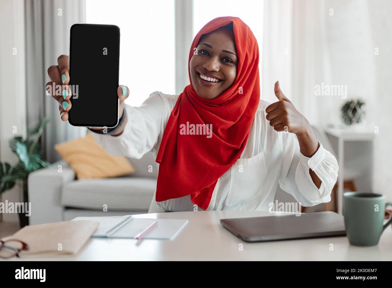 Application mobile sympa. Bonne femme musulmane afro-américaine montrant un smartphone avec un écran vierge et une okey gestante Banque D'Images