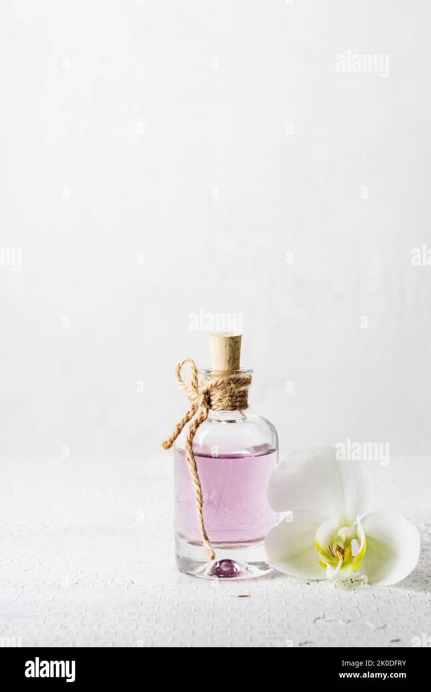 Huile essentielle de rose en bouteille de verre et fleur d'orchidée sur fond blanc. Banque D'Images
