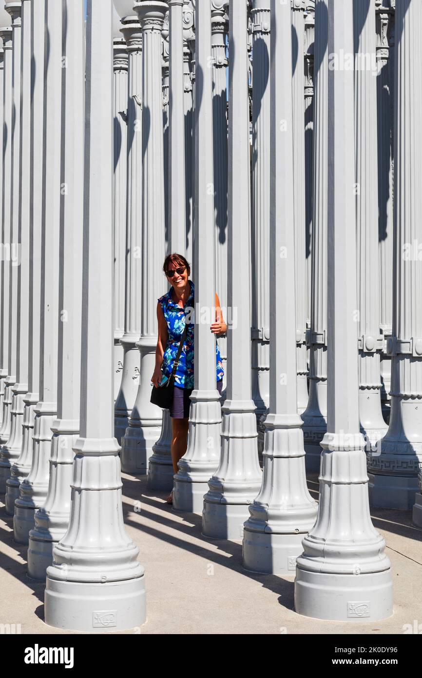 Une touriste féminine regarde derrière les lampadaires de l'exposition d'art publique de Chris Burden, Urban Lights, à l'entrée de la muse du comté de Los Angeles Banque D'Images