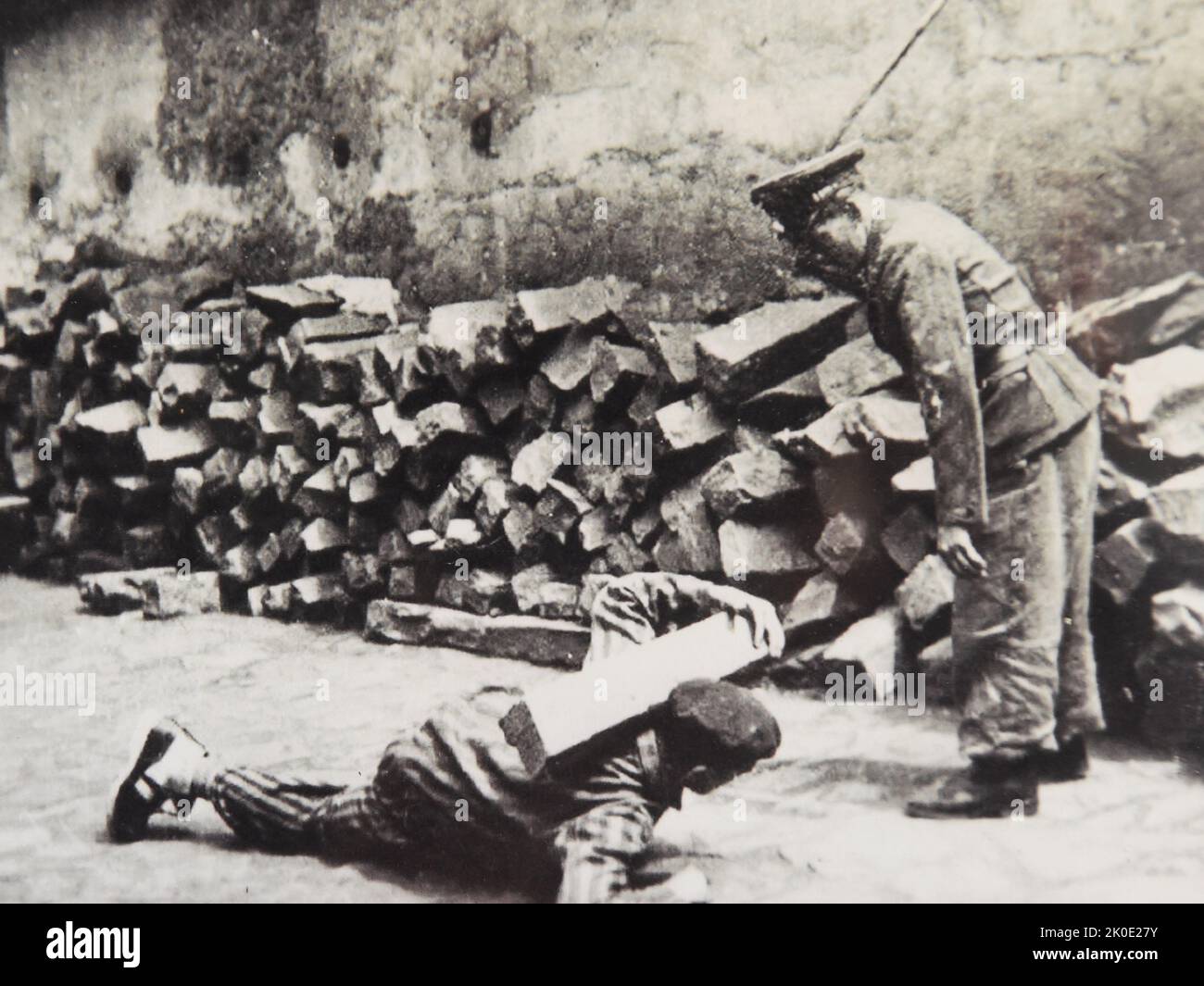 Un soldat SS dans un camp, regardant un détenu rampant devant lui portant un bloc de pierre sur ses épaules au camp de concentration de Muhlhausen en Allemagne, 1942. Banque D'Images