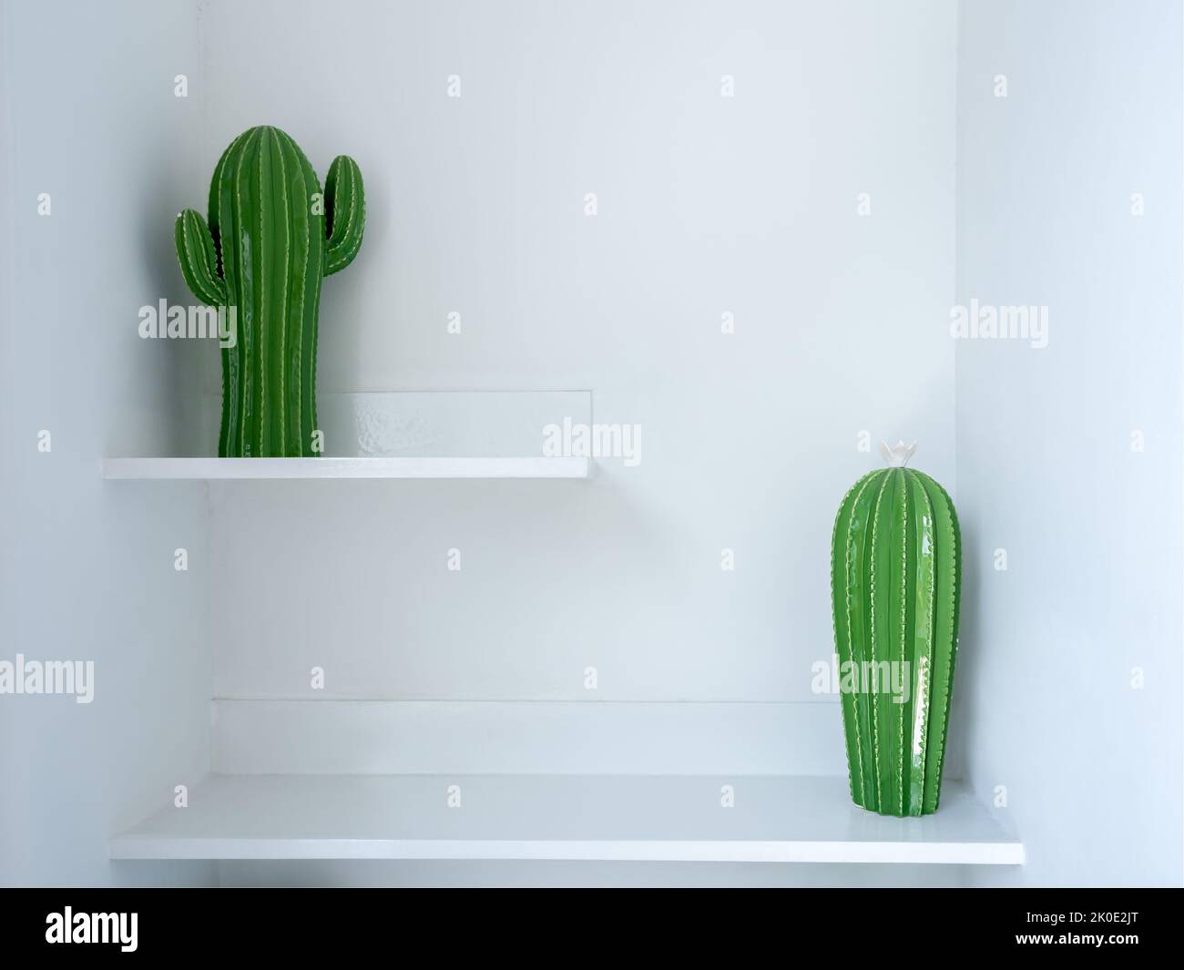 Deux décorations de modèle de poupée de cactus en céramique verte sur deux marches de tablette blanche. Décoration d'intérieur avec faux objet végétal. Banque D'Images