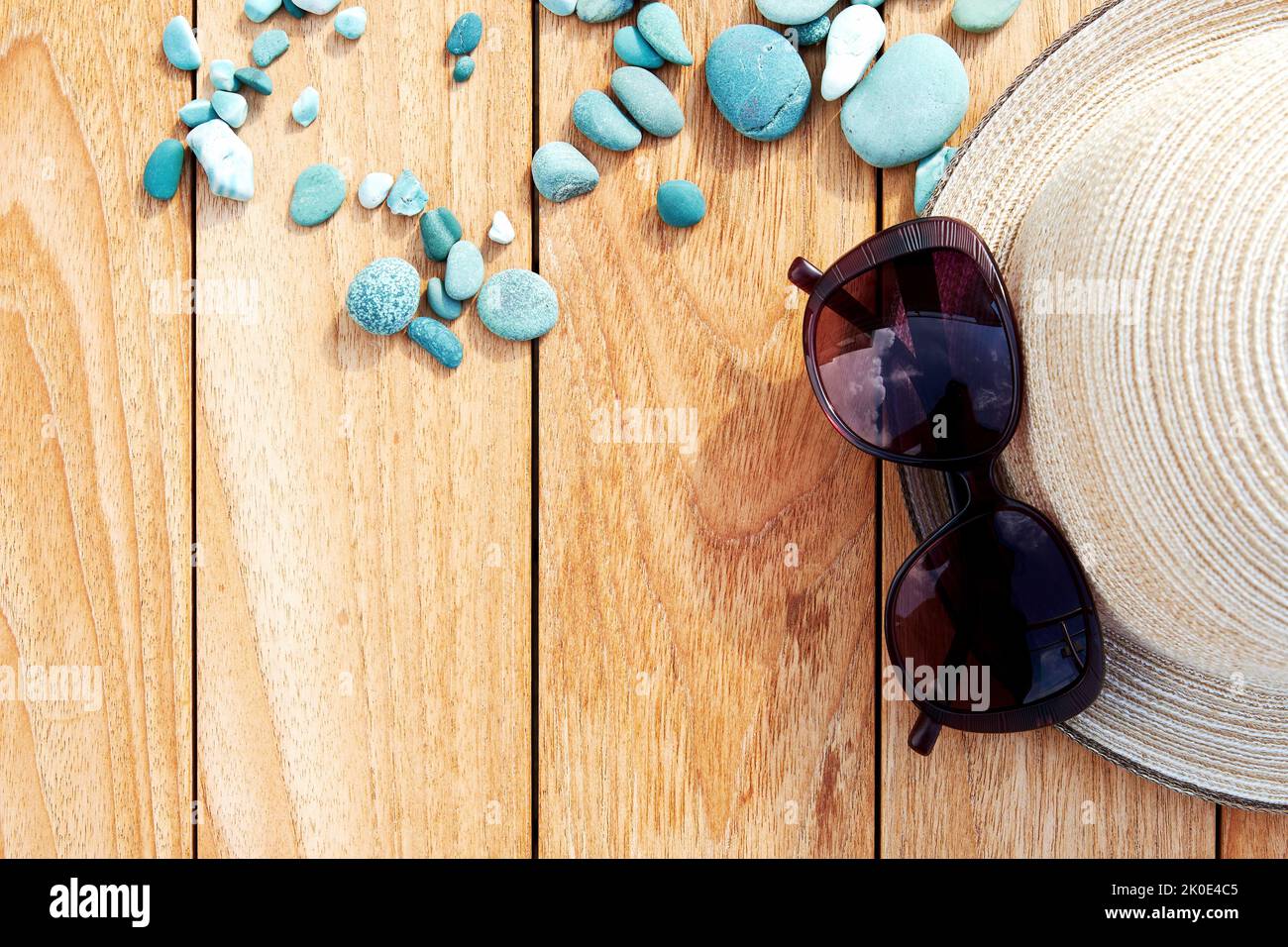 Plat avec chapeau de plage, lunettes de soleil et galets bleus sur la table en bois. Activités de loisirs en mer et accessoires de plage Banque D'Images