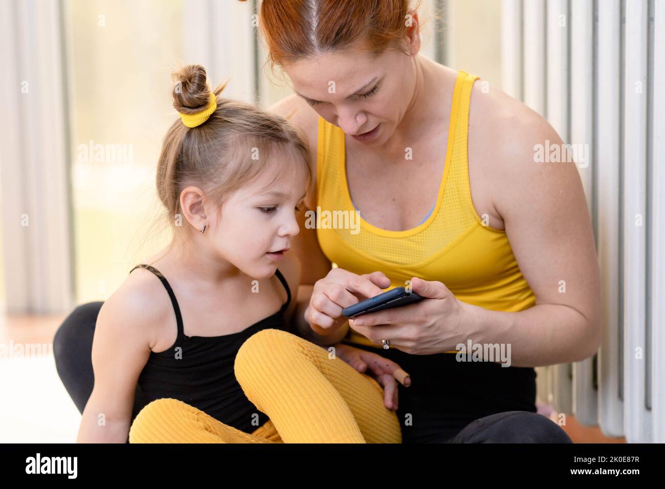 Jeune mère de forme ayant amour du temps avec sa fille, regardant un téléphone ensemble Banque D'Images