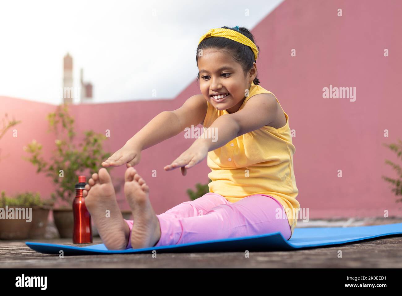 Une fille indienne pratiquant le yoga dans le visage souriant sur le tapis de yoga à l'extérieur Banque D'Images