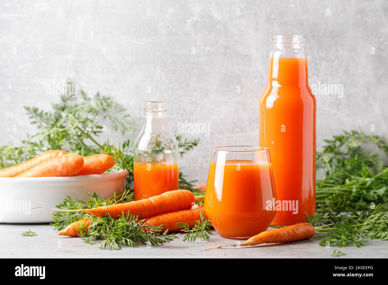 Jus de carottes dans un verre et une bouteille et carottes fraîches avec des feuilles Banque D'Images