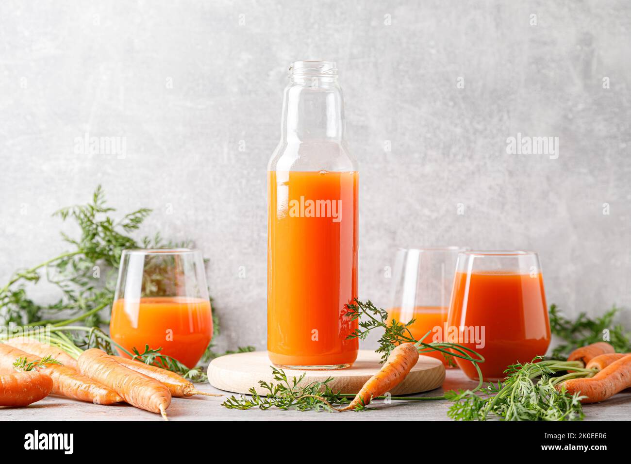 Jus de carottes dans un verre et une bouteille et carottes fraîches avec des feuilles Banque D'Images