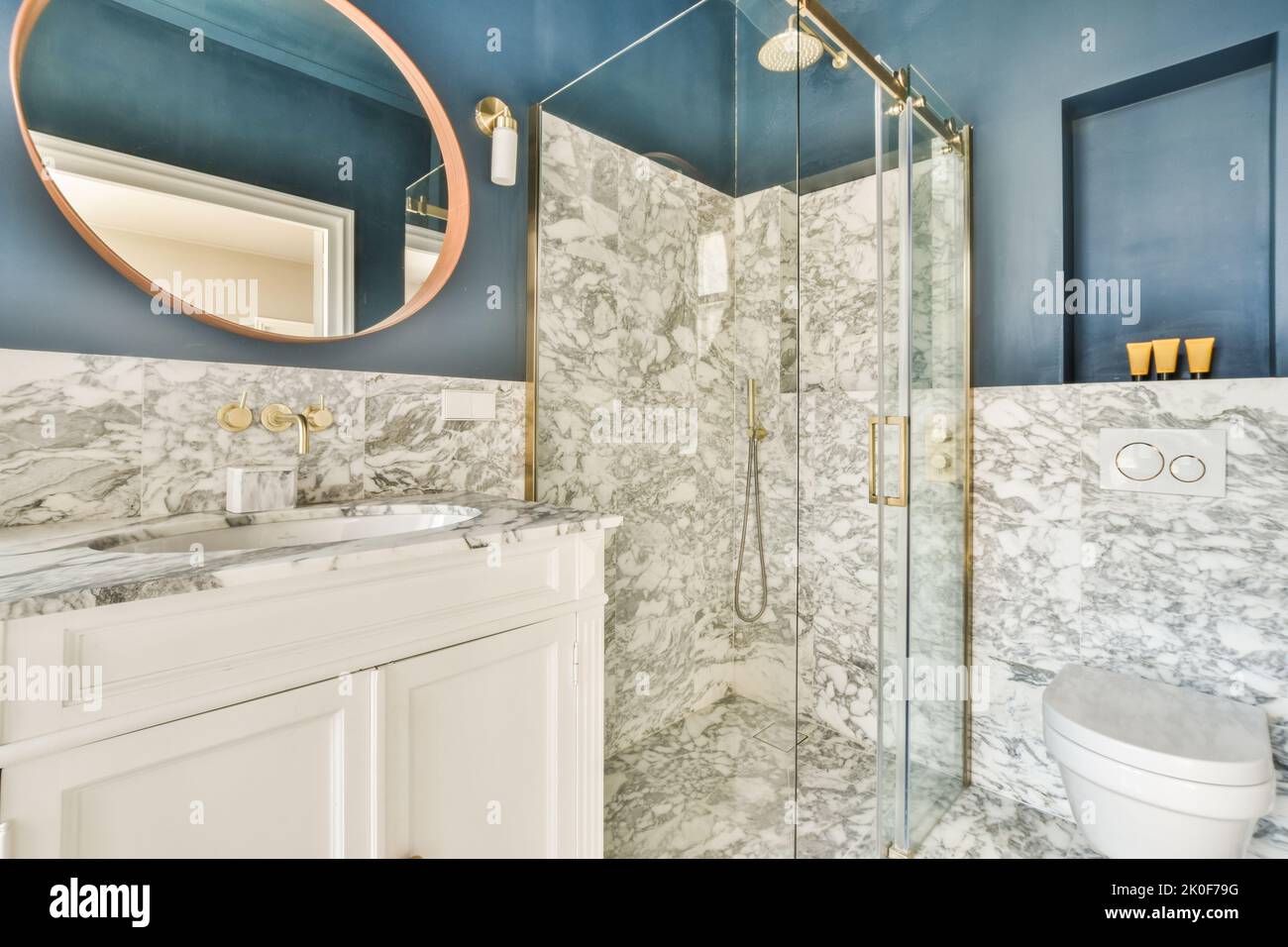 Baignoire avec douche en verre placée dans le coin près du lavabo et des toilettes dans une petite salle de bains lumineuse avec des murs en marbre Banque D'Images
