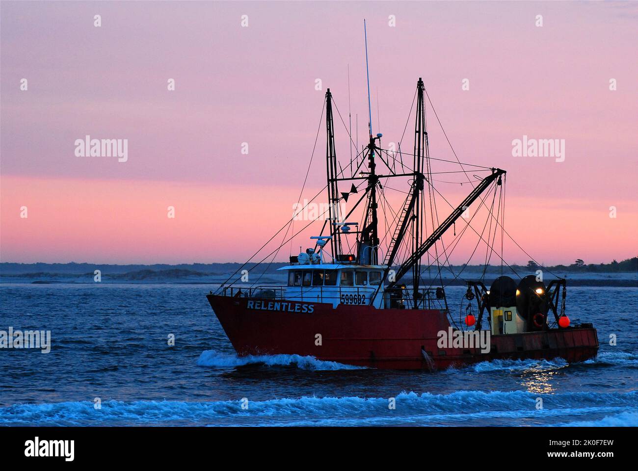 Un chalutier et un navire de pêche traversent le point d'entrée, sur le chemin du retour au port au lever du soleil Banque D'Images