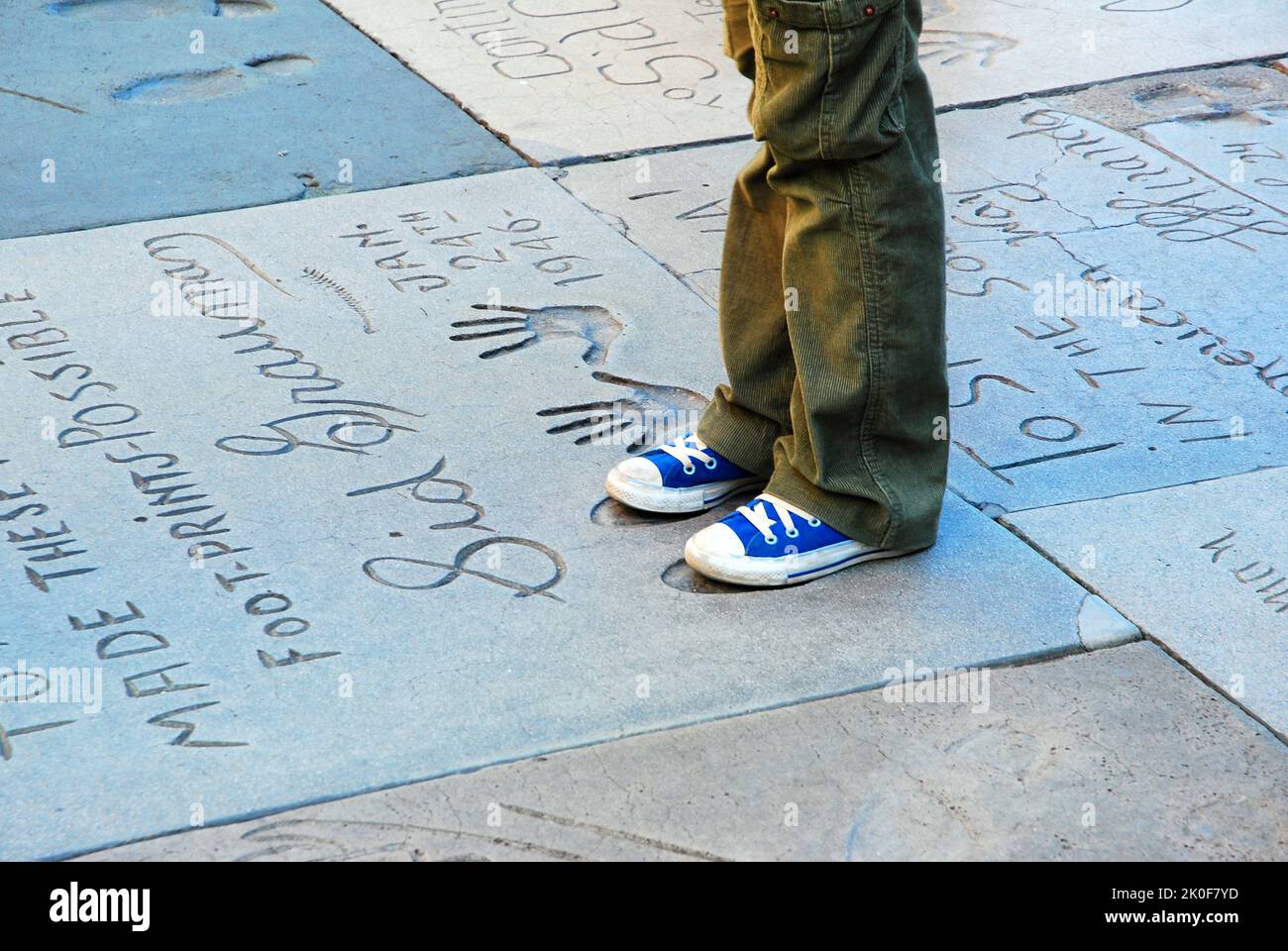 Un jeune garçon se taille les pieds dans les empreintes de célèbres stars du cinéma dans la cour avant du théâtre chinois de Graumans à Hollywood Banque D'Images