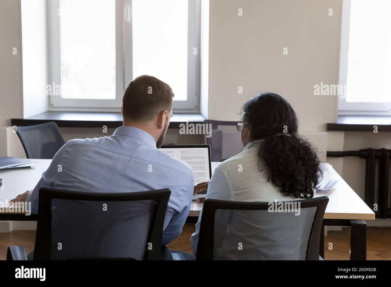 Deux employés multiethniques partageant un ordinateur portable à table Banque D'Images