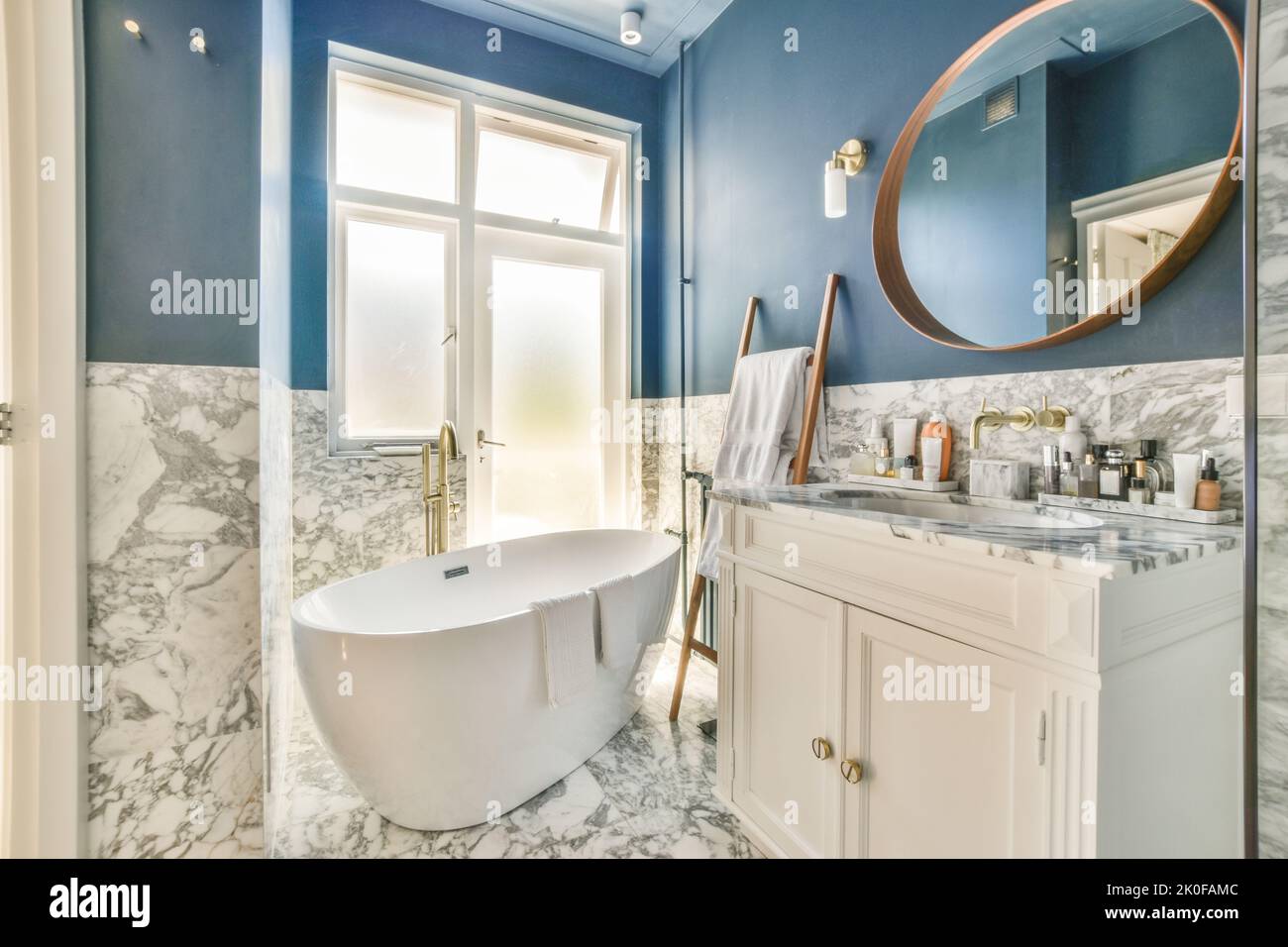 Baignoire avec douche en verre placée dans le coin près du lavabo et des toilettes dans une petite salle de bains lumineuse avec des murs en marbre Banque D'Images