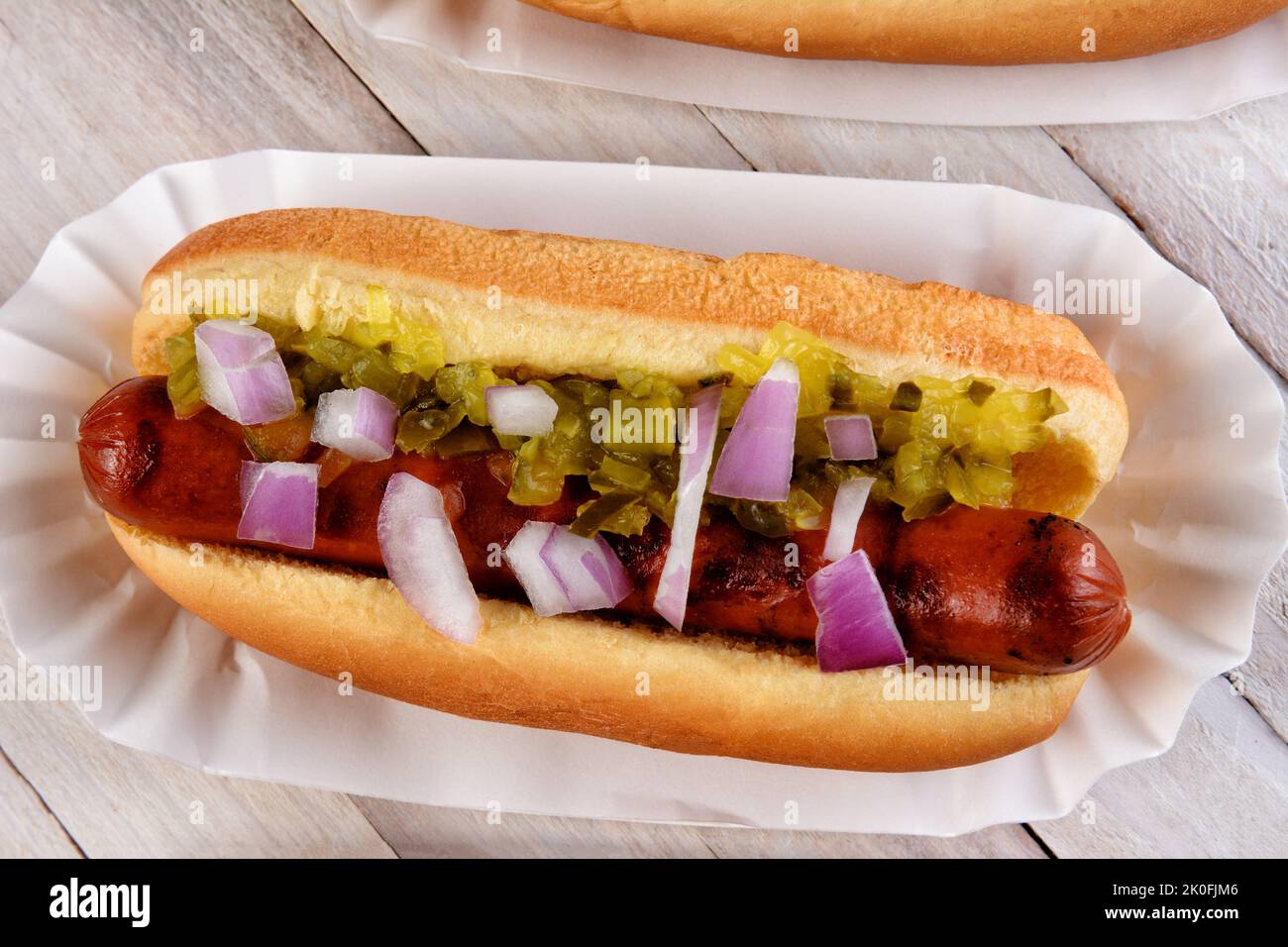 Photo aérienne d'un Hot Dog avec des oignons et relish sur une table de pique-nique rustique en bois blanc. Banque D'Images