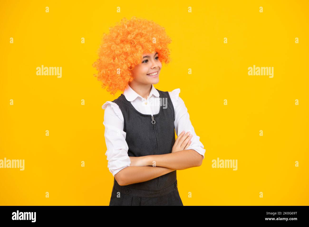 Anniversaire fête d'enfants. Drôle d'enfant dans la perruque clown curly isolé sur fond jaune. Visage de fille heureux, émotions positives et souriantes. Banque D'Images
