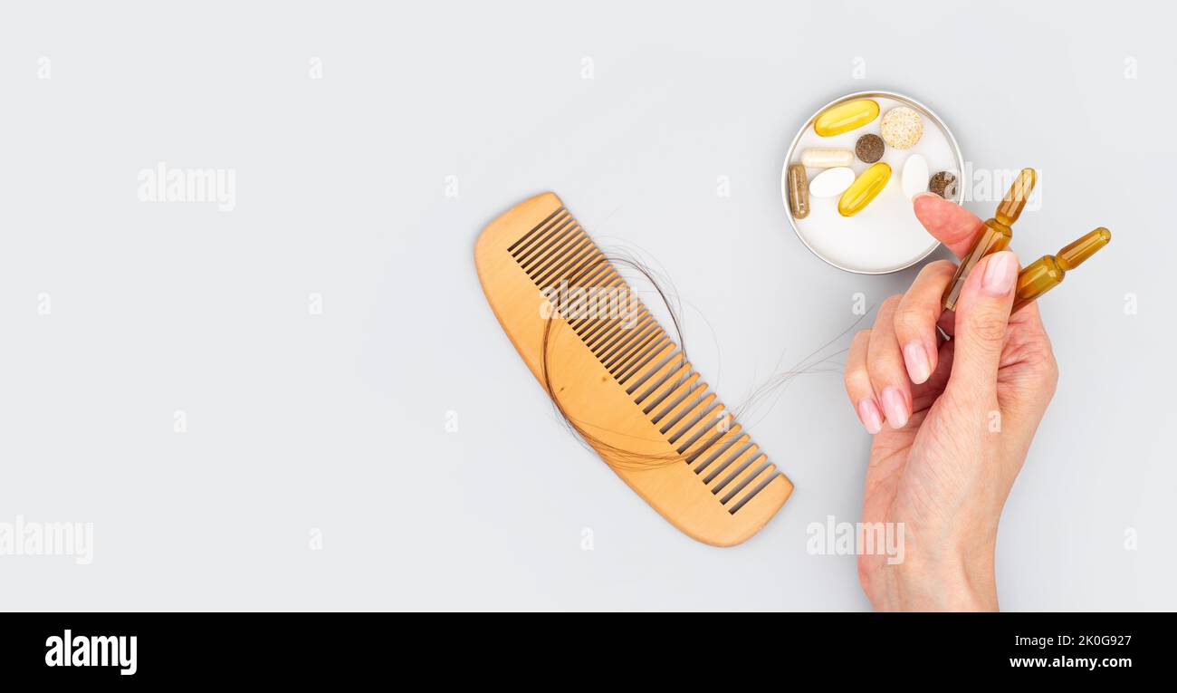 Ampoules cosmétiques contenant du sérum dans la main féminine, vitamines pour la croissance des cheveux, restauration des cheveux de beauté. Peigne en bois avec perte de cheveux sur fond gris. Banque D'Images
