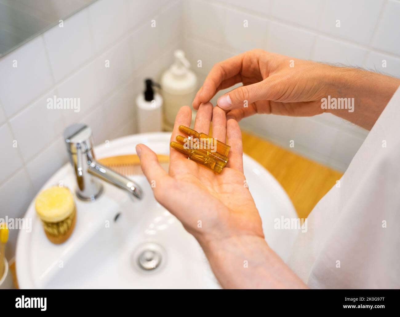 Mains de sexe masculin tenant des ampoules cosmétiques avec du sérum pour la croissance des cheveux, la restauration des cheveux de beauté dans une salle de bains moderne et lumineuse. Concept perte de cheveux Banque D'Images