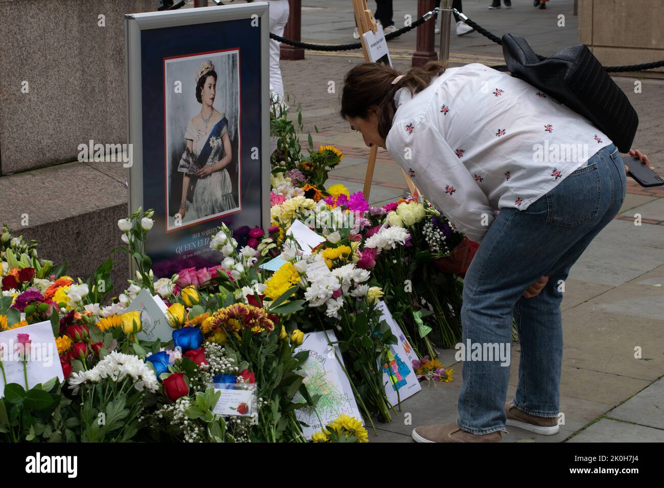 Femme regardant des fleurs devant le portrait de la reine Elizabeth II sur la place Saint-Anns. Hommage officiel à la Reine après sa mort. Manchester. Banque D'Images