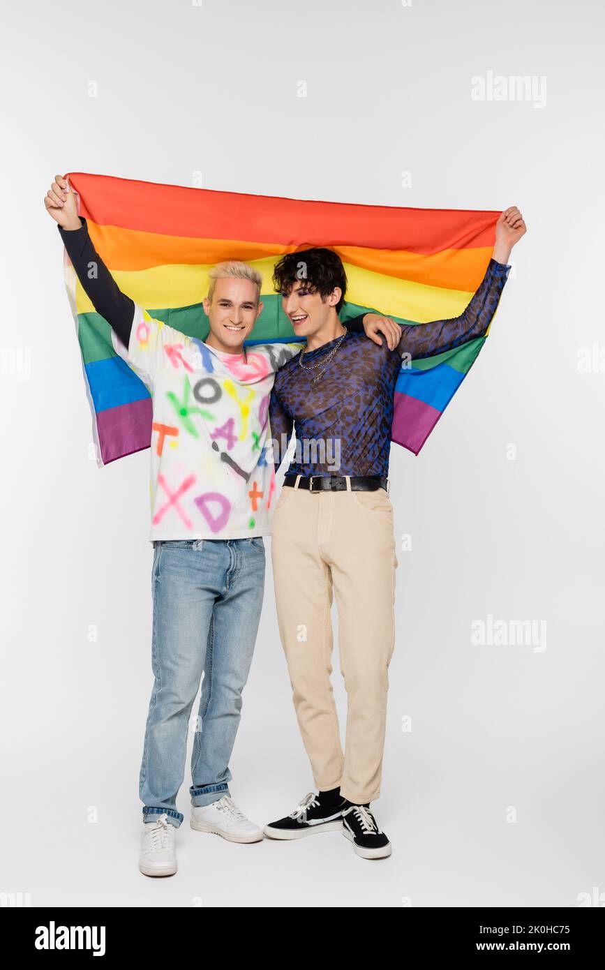pleine longueur d'homme gay et de personne non binaire tenant le drapeau lgbtq sur fond gris, image de stock Banque D'Images