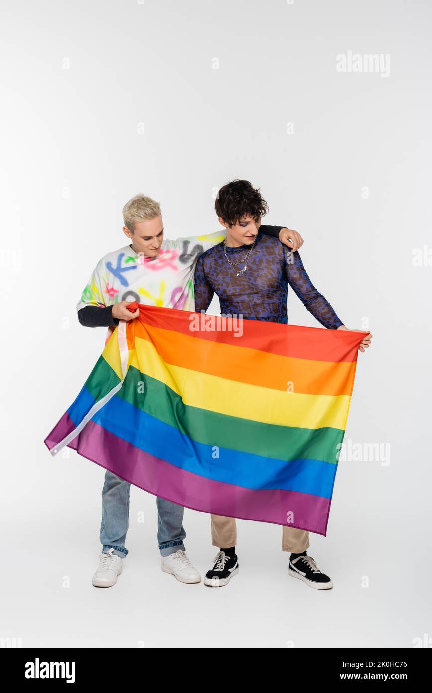 homme gay blond et brunette personne non binaire debout avec le drapeau lgbtq sur fond gris, image de stock Banque D'Images