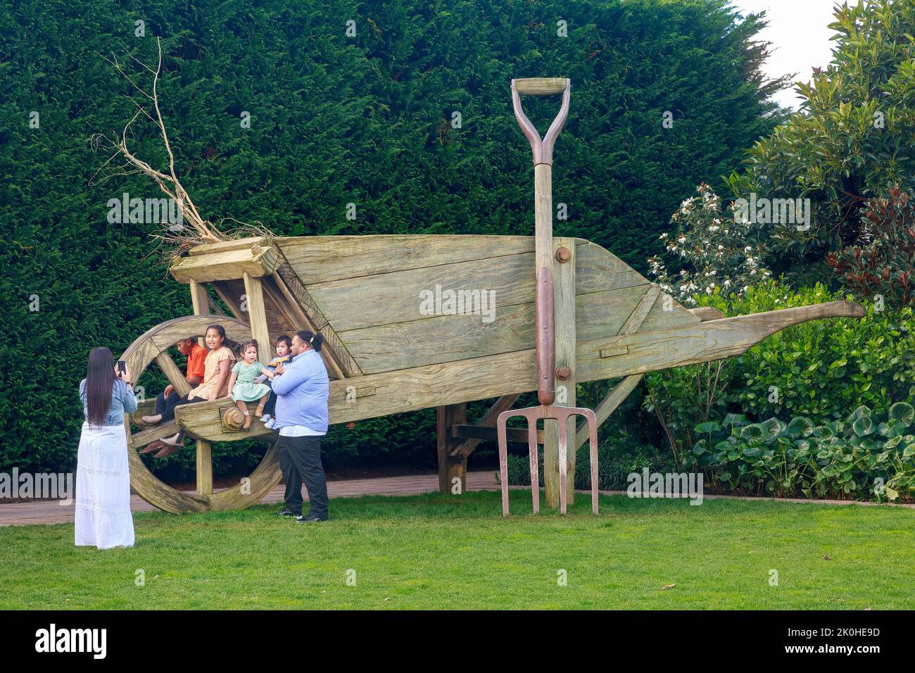 Une famille pose à côté d'une brouette géante dans le jardin surréaliste, l'un des jardins à thème du parc Hamilton Gardens, Hamilton, Nouvelle-Zélande Banque D'Images