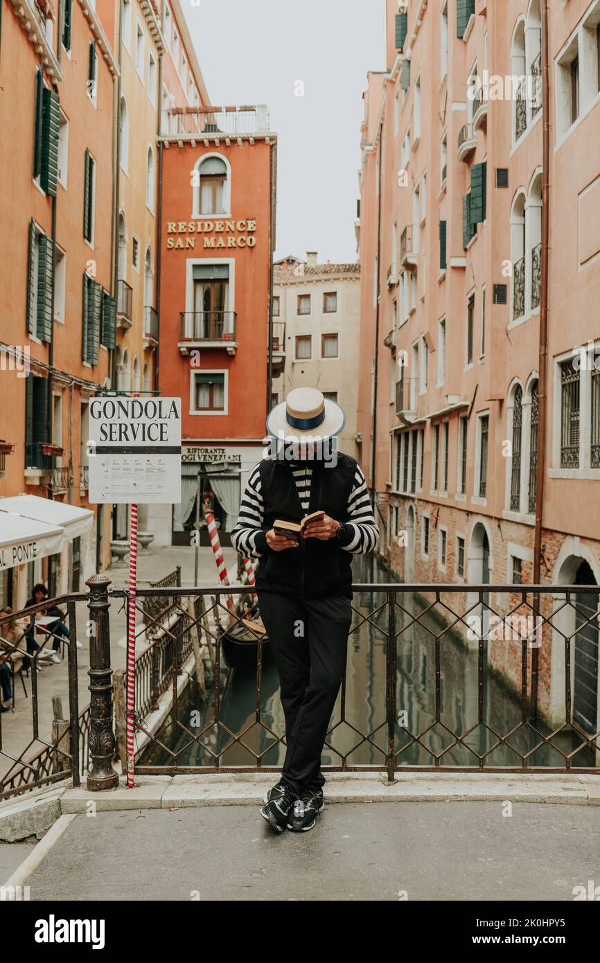Une verticale d'un gondolier lisant un livre sur un pont au-dessus d'un canal à Venise, en Italie Banque D'Images