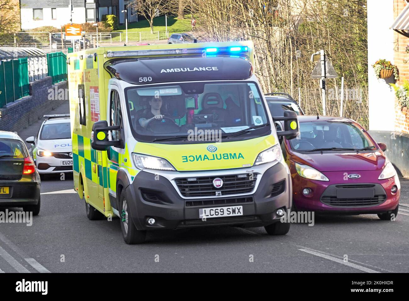 Vue rapprochée de l'avant de Fiat NHS bleu ambulance d'urgence surpassant la file d'attente suivie d'une voiture de police à Billericay High Street, Angleterre, Royaume-Uni Banque D'Images