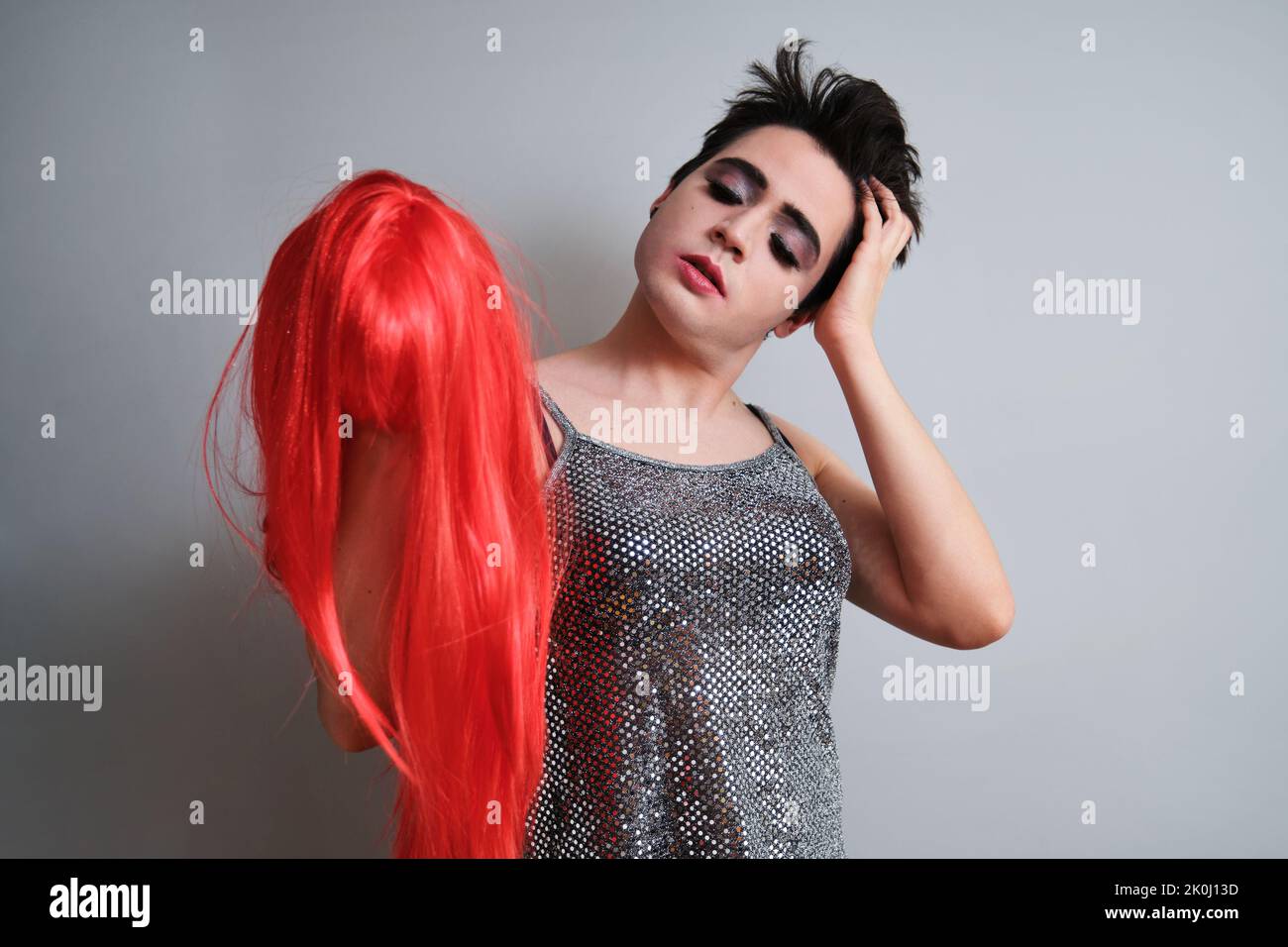Portrait de la personne transgenre qui prend la perruque rouge et regarde l'appareil photo. Banque D'Images