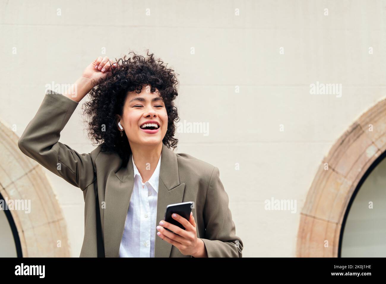 une femme heureuse avec des écouteurs sans fil riant écouter de la musique et danser avec son téléphone, concept de la jeunesse et de la technologie, espace de copie pour le texte Banque D'Images