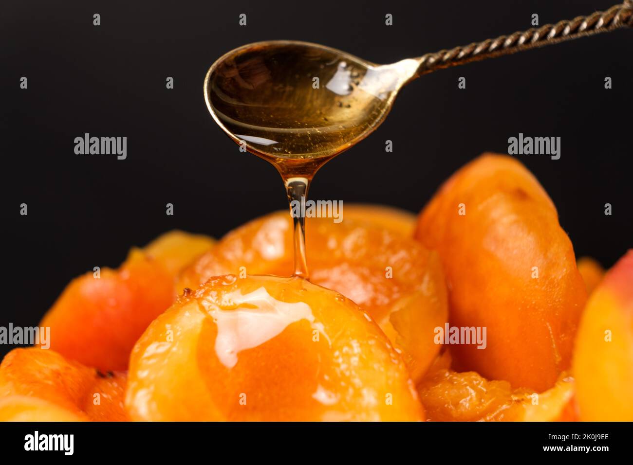 Le miel coule d'une cuillère sur des tranches d'abricots juteux sur fond noir. Banque D'Images