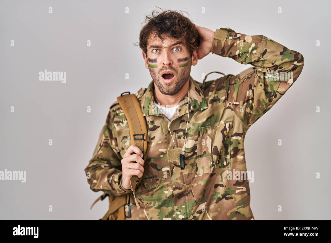 Jeune homme hispanique portant un uniforme militaire de camouflage fou et effrayé avec les mains sur la tête, peur et surpris de choc avec la bouche ouverte Banque D'Images