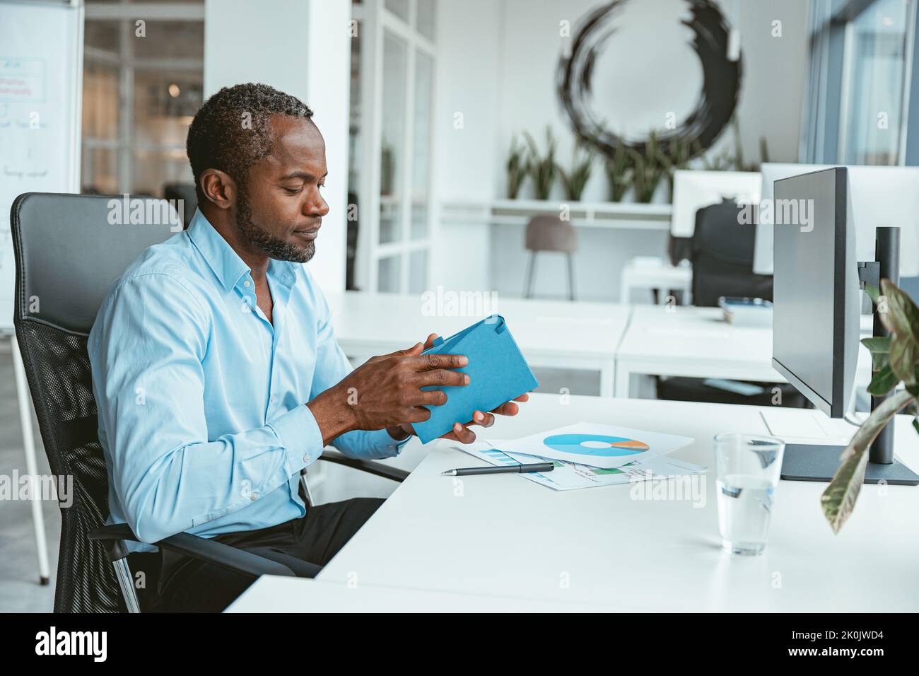 Homme d'affaires africain travaillant avec des documents tout en étant assis dans un bureau moderne Banque D'Images