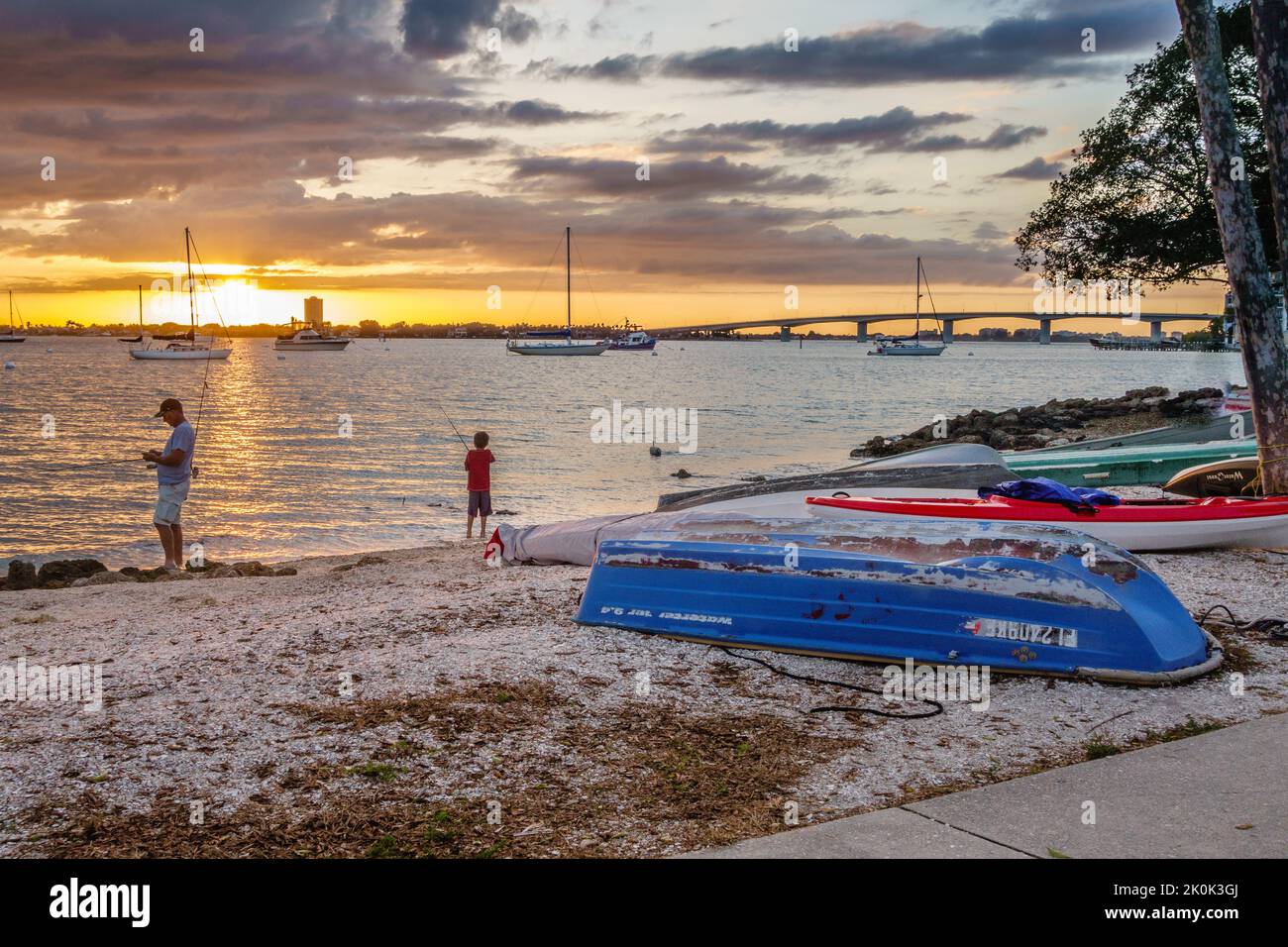 Sarasota, FL, US-30 mai 2022 : silhouette de père et de fils pêchant au coucher du soleil avec de vieux bateaux sur la plage avec un ciel spectaculaire Banque D'Images