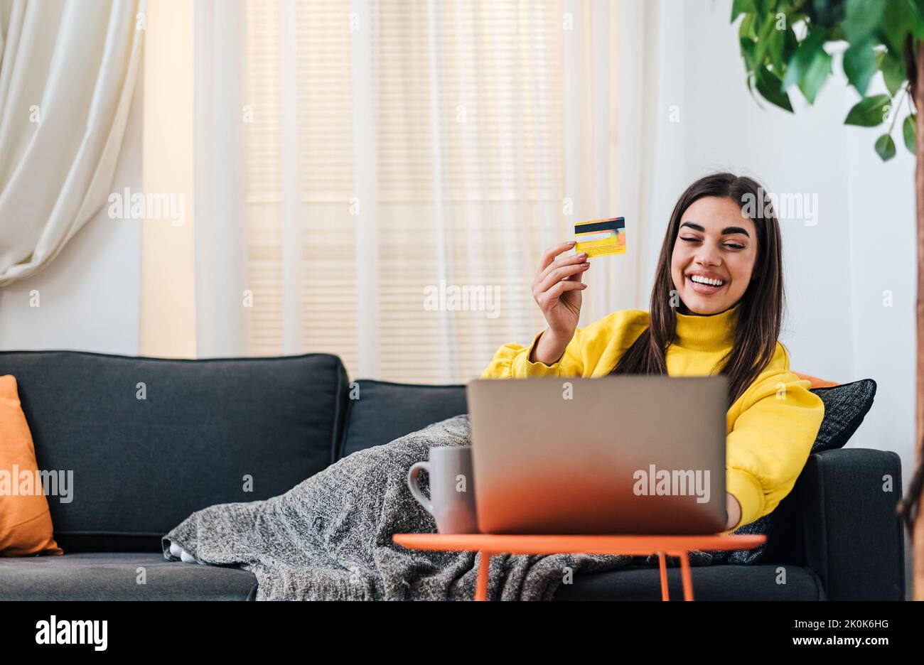 Ravie jeune femme brune, tenant sa carte de crédit, vérifiant son compte bancaire du lit sur ordinateur portable. Banque D'Images