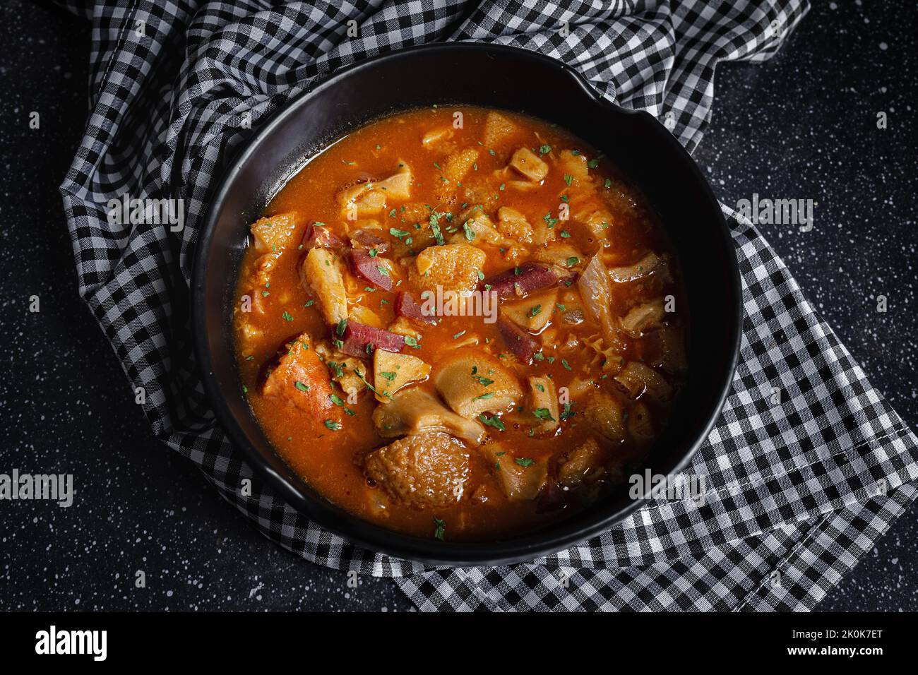 De dessus de savoureux callos a la madrilena dans un bol noir sur la table avec serviette Banque D'Images