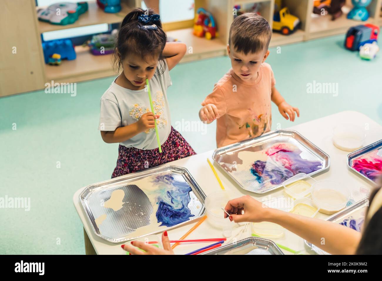 École maternelle multiculturelle. Les tout-petits jouant avec des pailles rayées et la peinture au lait, en utilisant des colorants alimentaires non toxiques pour les couleurs. Activité créative des enfants pour utiliser leurs sens et le développement du cerveau. Peinture au doigt. Photo de haute qualité Banque D'Images