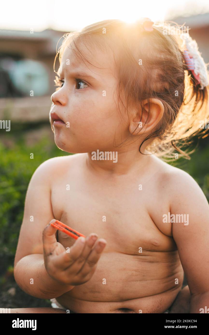 Bébé curieux fille tenant quelque chose qu'elle a trouvé creuser dans le jardin dans la cour de la maison. Le concept est l'éducation, le développement précoce de l'enfant Banque D'Images