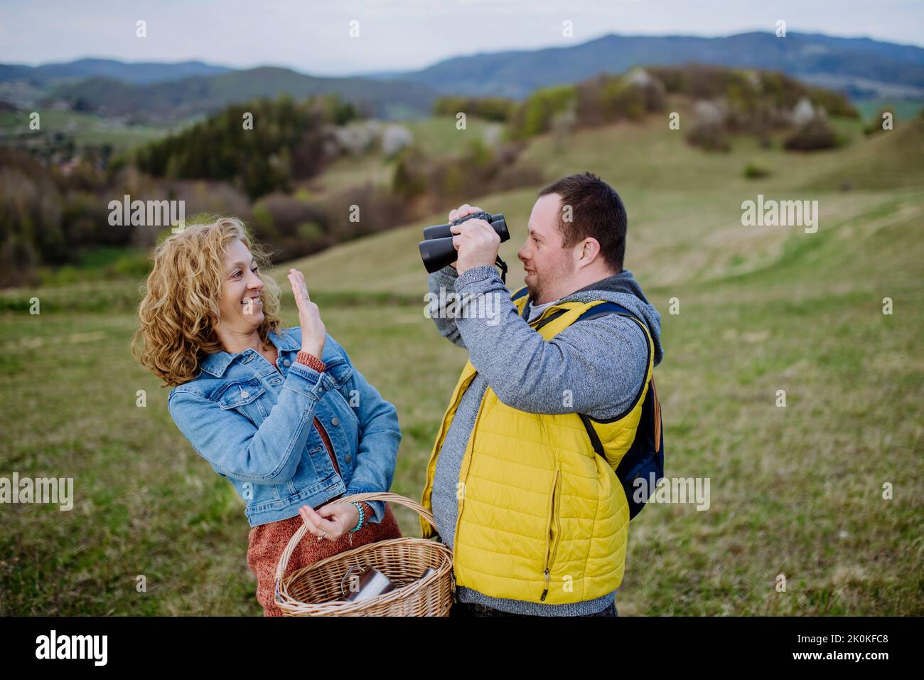 Jeune homme heureux avec le syndrome de Down avec sa mère se reposant dans la nature, assis et regardant avec des jumelles. Banque D'Images