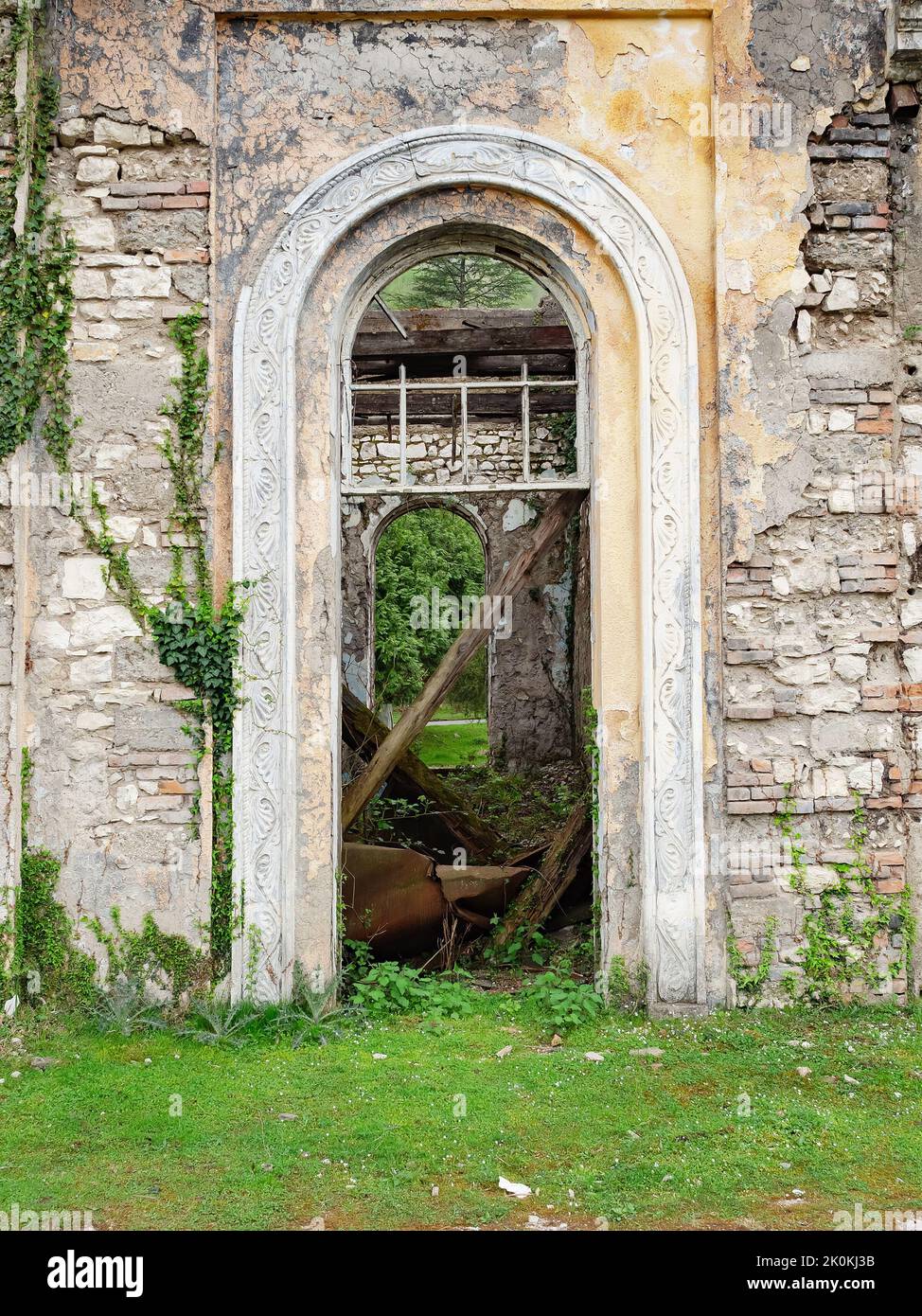 Vue à travers la porte voûtée d'une fenêtre cassée dans un vieux bâtiment abandonné surcultivé Banque D'Images