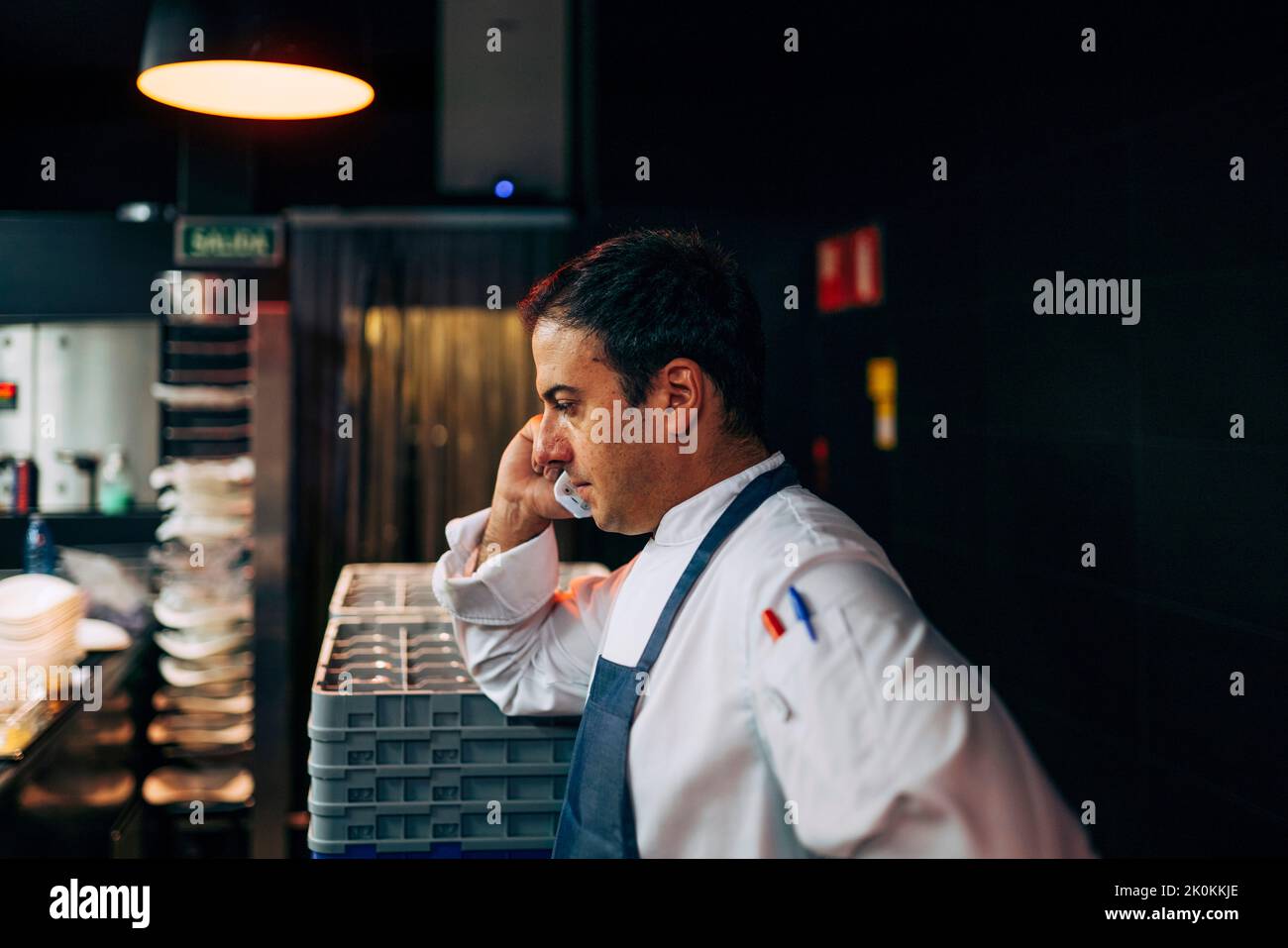 Vue latérale de l'homme travaillant dans la cuisine du restaurant et ayant un appel téléphonique Banque D'Images
