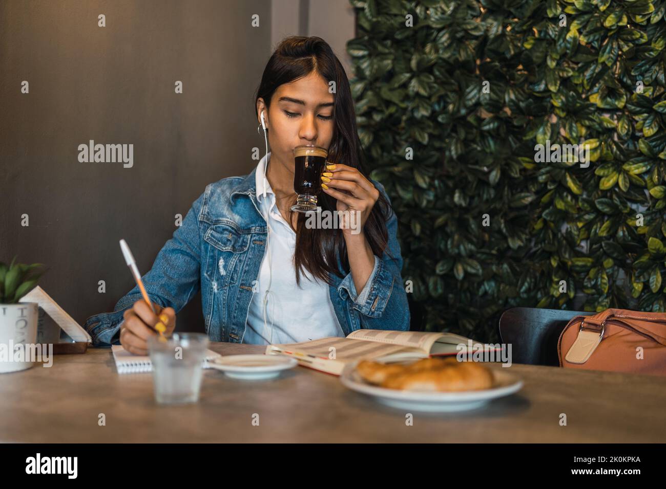 Contenu intelligent jeune hispanique étudiante écrire dans le livre d'auteur tout en faisant devoirs à la table boire du café Banque D'Images