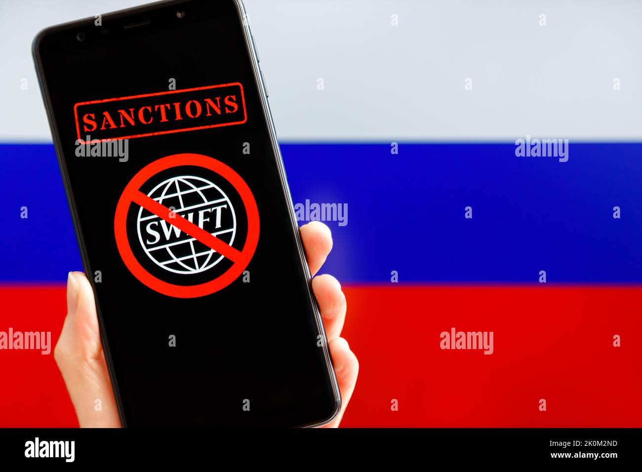 Ukraine, Kiev - février, 23 2022: Main tenant mobile avec le logo SWIFT barré et le drapeau russe en arrière-plan. Sanctions contre la Russie, déconnexion du concept SWIFT. Banque D'Images