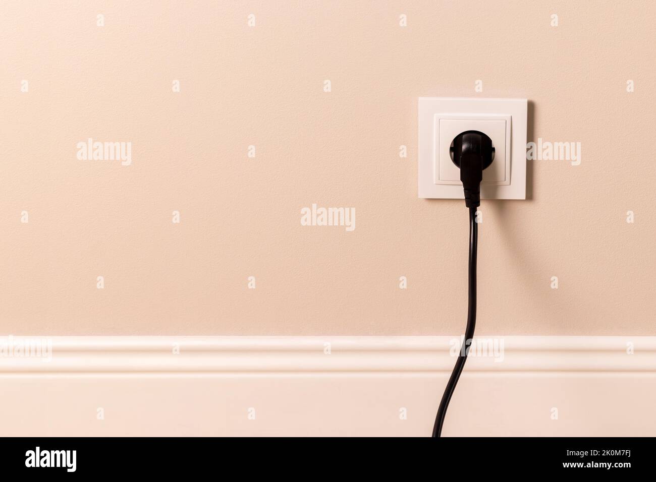 Prise électrique européenne blanche avec fiche noire insérée sur un mur beige moderne Banque D'Images