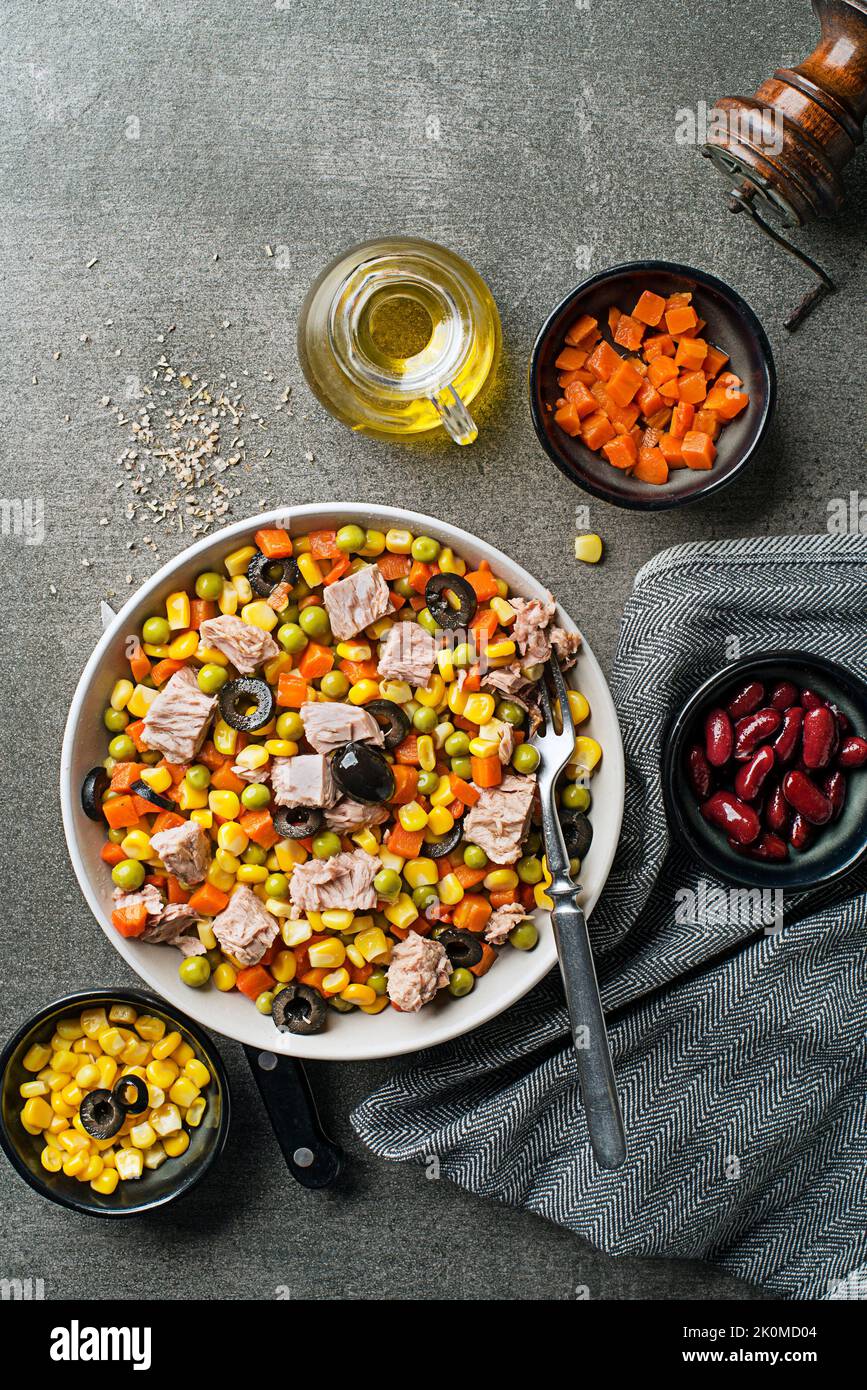 Salade de thon mixte saine avec cornes, carottes, petits pois, haricots et olives sur fond de table gris. Salade de maïs mexicaine. Banque D'Images